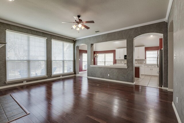 unfurnished living room featuring dark wood-type flooring, ornamental molding, and ceiling fan with notable chandelier