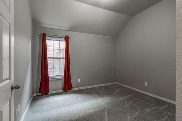 carpeted spare room featuring lofted ceiling and baseboards