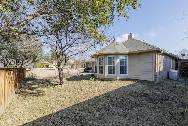 rear view of property featuring a shingled roof, a fenced backyard, brick siding, and a chimney