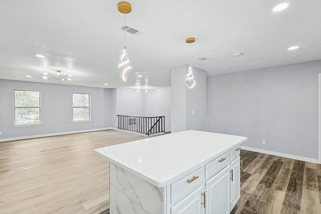 kitchen featuring white cabinetry, hanging light fixtures, a center island, light stone counters, and light hardwood / wood-style flooring