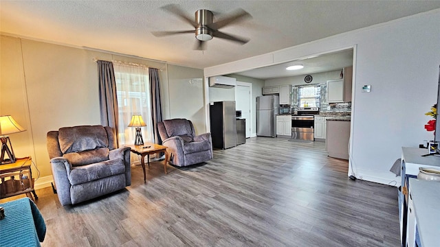 living room with a wall mounted air conditioner, a textured ceiling, hardwood / wood-style floors, and ceiling fan