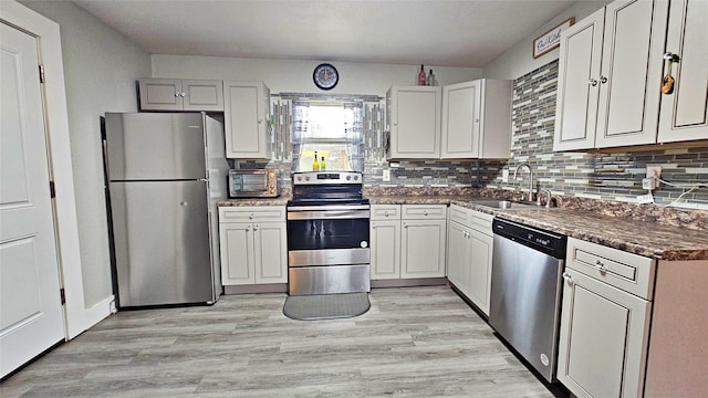 kitchen featuring sink, stainless steel appliances, white cabinets, decorative backsplash, and light wood-type flooring