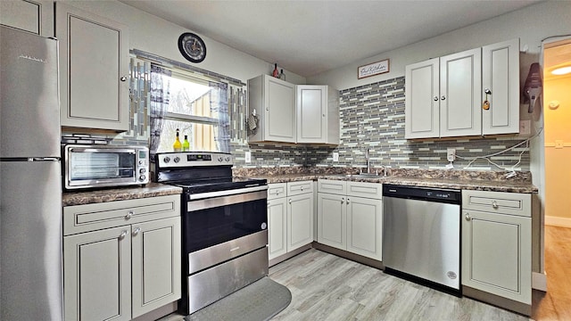 kitchen featuring appliances with stainless steel finishes, sink, light hardwood / wood-style flooring, and backsplash