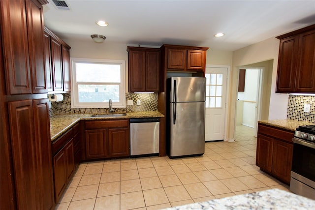 kitchen with sink, light tile patterned floors, appliances with stainless steel finishes, stone countertops, and decorative backsplash