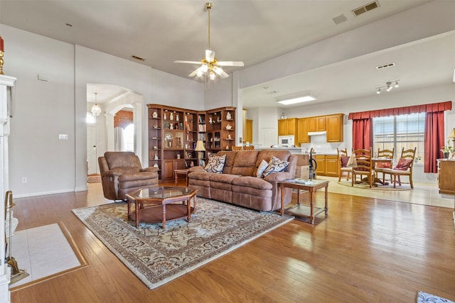 living room with light hardwood / wood-style floors, ceiling fan, and ornate columns