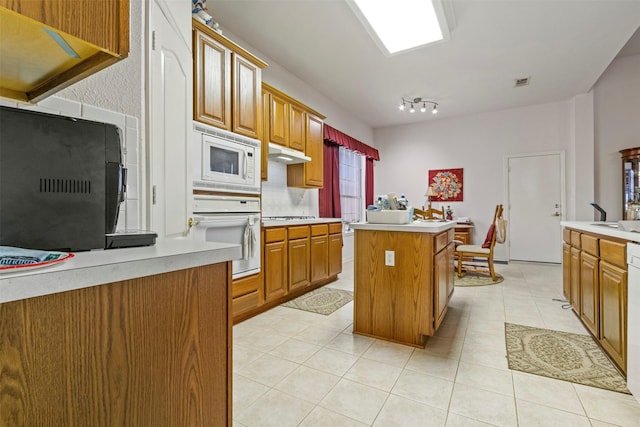 kitchen with backsplash, white appliances, a center island, and light tile patterned flooring