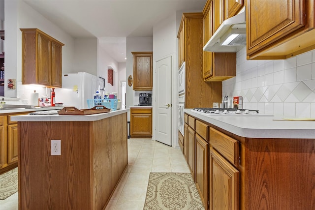 kitchen featuring tasteful backsplash, light tile patterned floors, white appliances, and a center island