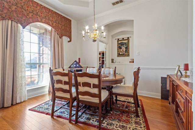 dining space with an inviting chandelier, ornamental molding, and light wood-type flooring