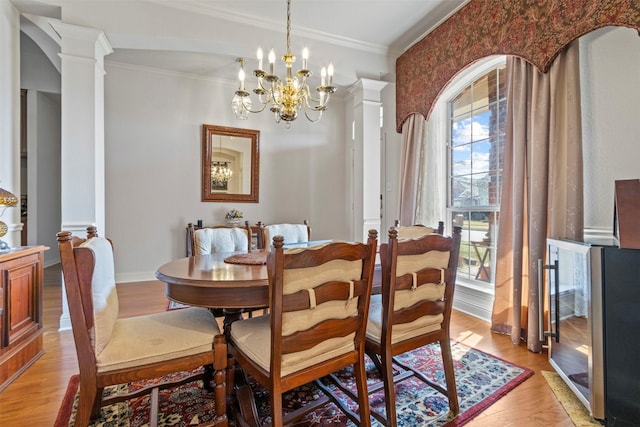 dining area featuring decorative columns, crown molding, a chandelier, and light wood-type flooring