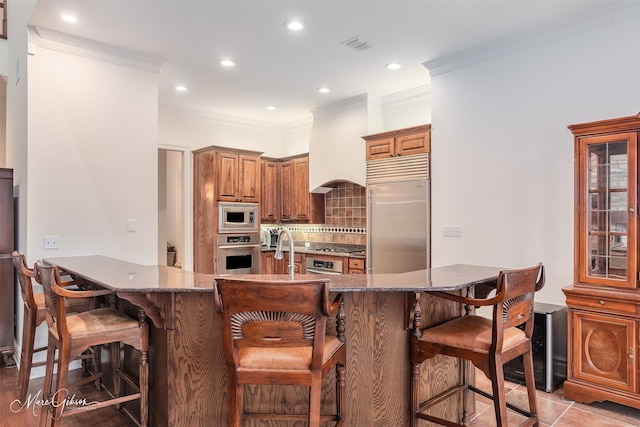 kitchen with sink, a breakfast bar area, premium range hood, built in appliances, and decorative backsplash