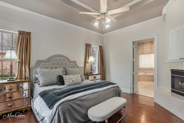 bedroom with a tile fireplace, dark hardwood / wood-style flooring, ornamental molding, ceiling fan, and ensuite bath