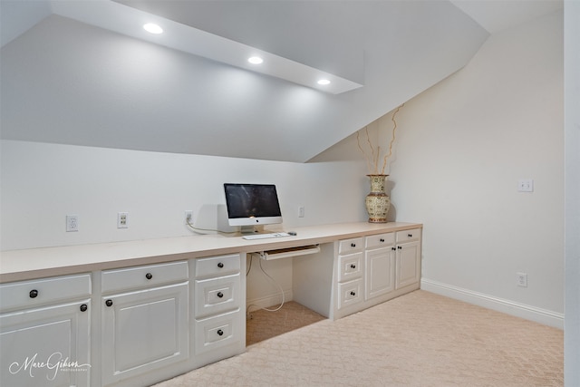 unfurnished office featuring lofted ceiling, built in desk, and light colored carpet