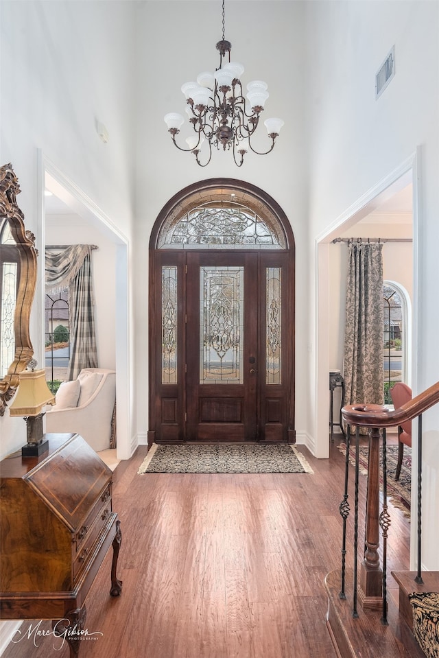 entryway with a notable chandelier, a towering ceiling, and wood-type flooring