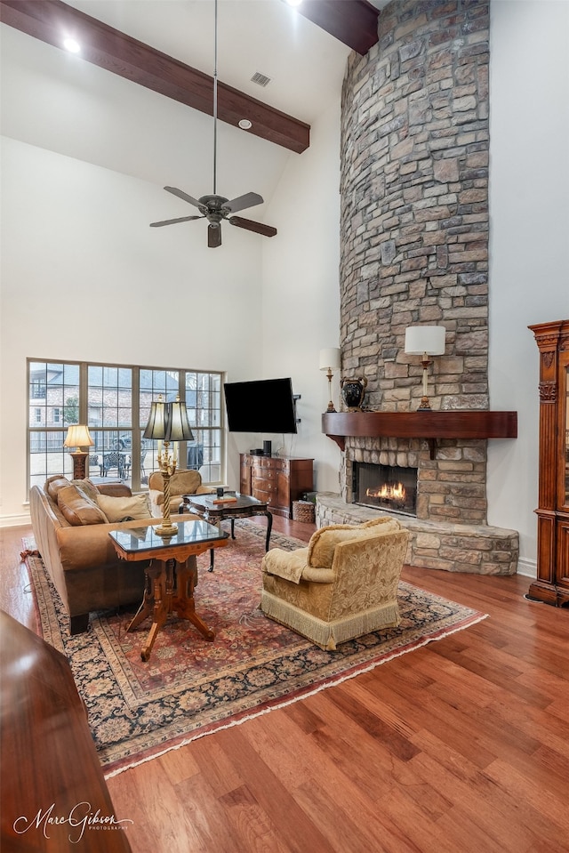 living room with ceiling fan, a high ceiling, a fireplace, wood-type flooring, and beamed ceiling