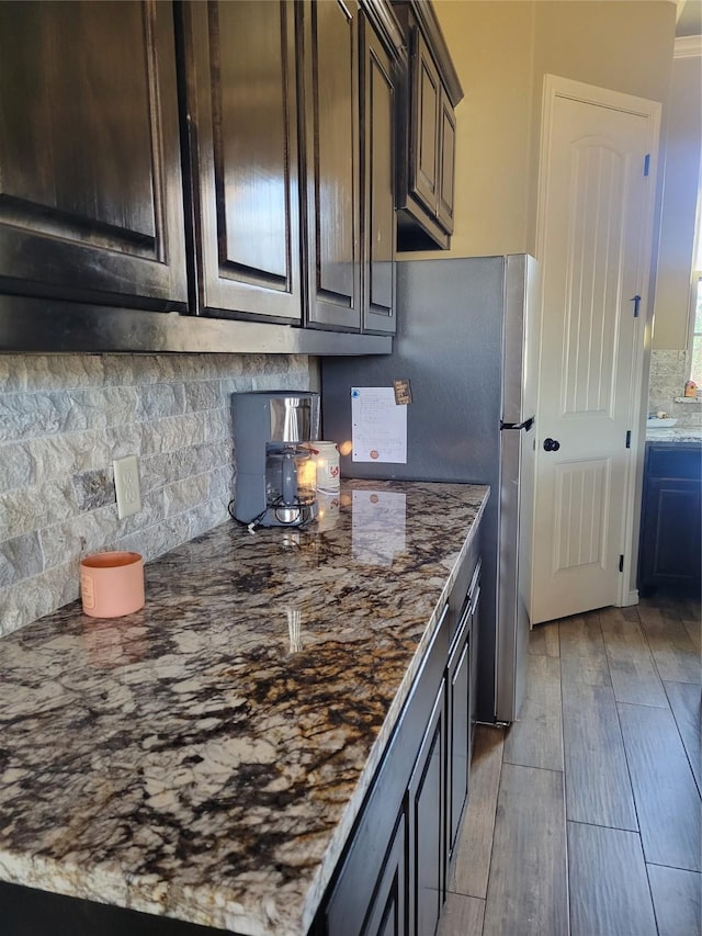 kitchen featuring tasteful backsplash, dark stone counters, dark brown cabinets, and light wood-type flooring