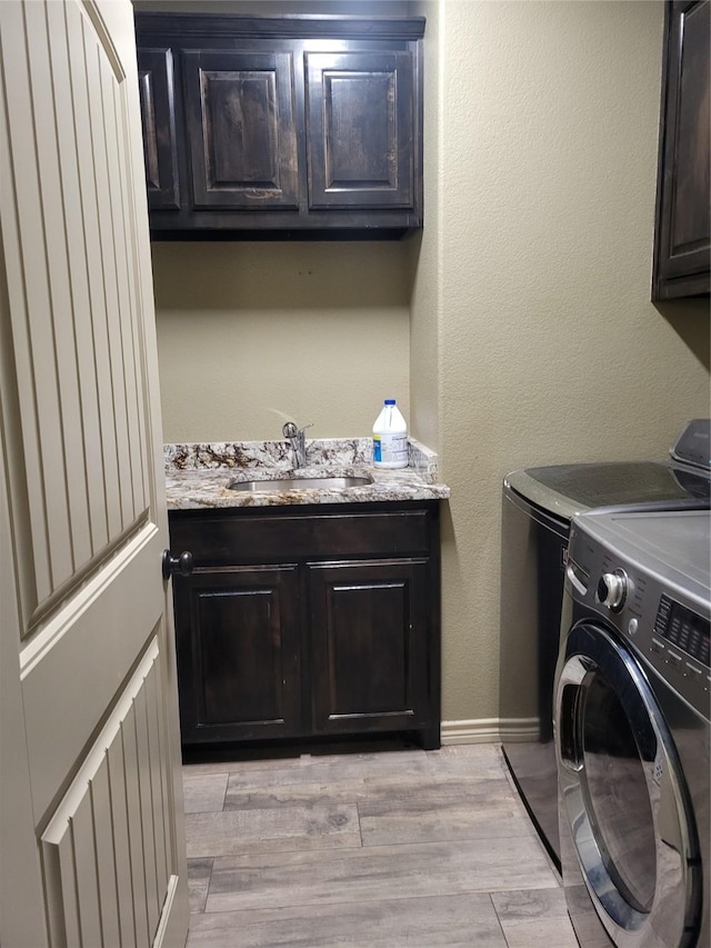 washroom with sink, light hardwood / wood-style floors, cabinets, and washing machine and clothes dryer