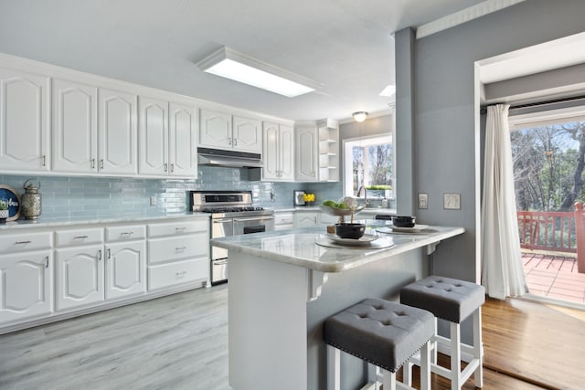 kitchen with a breakfast bar, white cabinetry, backsplash, double oven range, and kitchen peninsula