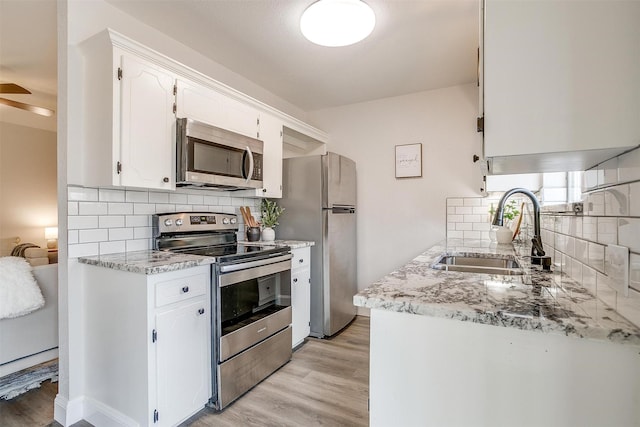 kitchen featuring appliances with stainless steel finishes, sink, white cabinets, decorative backsplash, and light wood-type flooring