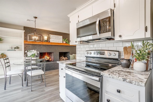 kitchen featuring backsplash, stainless steel appliances, a fireplace, white cabinets, and decorative light fixtures