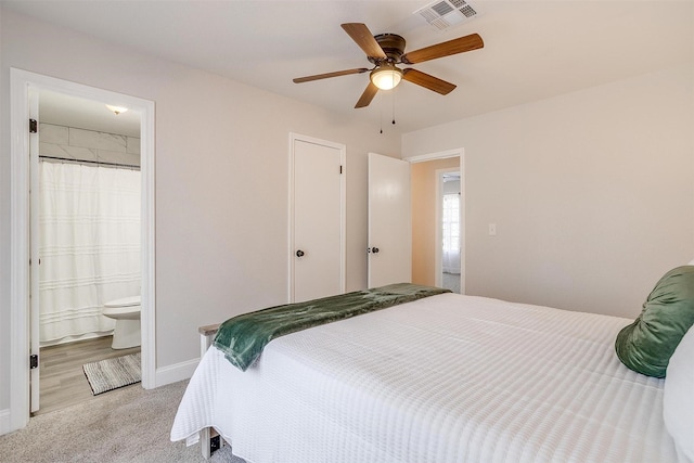 bedroom with ceiling fan, light colored carpet, and ensuite bath