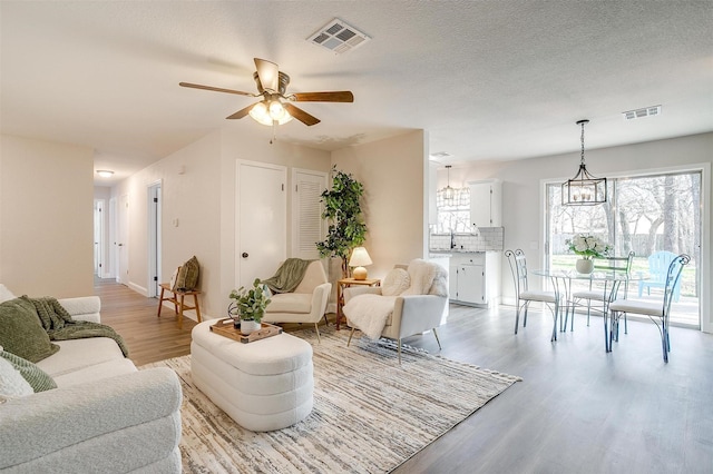 living room with sink, ceiling fan with notable chandelier, a textured ceiling, and light wood-type flooring