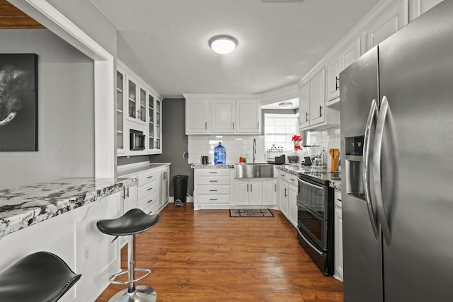 kitchen with white cabinetry, double oven range, stainless steel fridge, and light stone counters