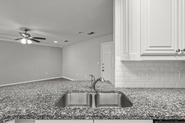 kitchen featuring sink, white cabinets, backsplash, dark stone counters, and a textured ceiling