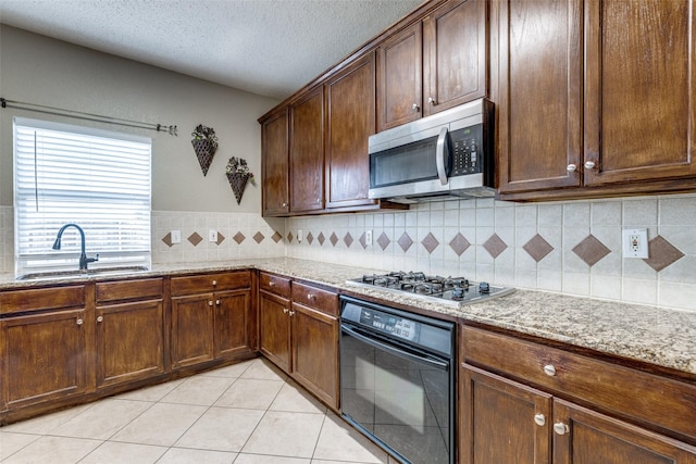 kitchen featuring light tile patterned flooring, stainless steel appliances, light stone countertops, and sink