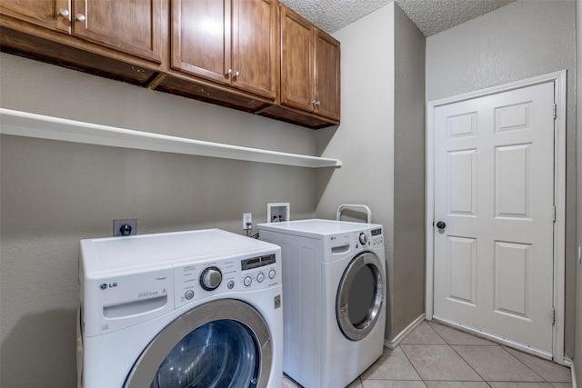 washroom with light tile patterned flooring, cabinets, washing machine and dryer, and a textured ceiling