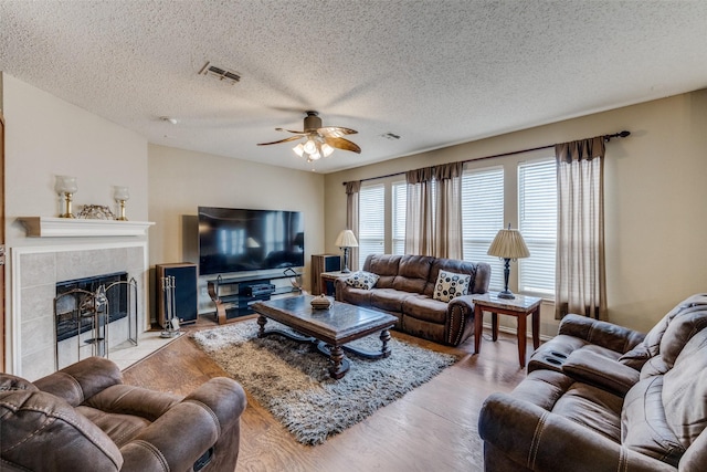 living room featuring ceiling fan, light hardwood / wood-style floors, a tile fireplace, and a textured ceiling