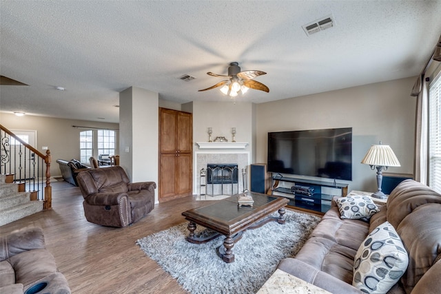 living room with wood-type flooring, ceiling fan, a fireplace, and a textured ceiling