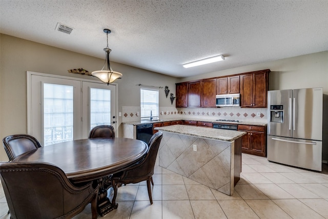 kitchen with tasteful backsplash, light tile patterned floors, appliances with stainless steel finishes, pendant lighting, and light stone countertops