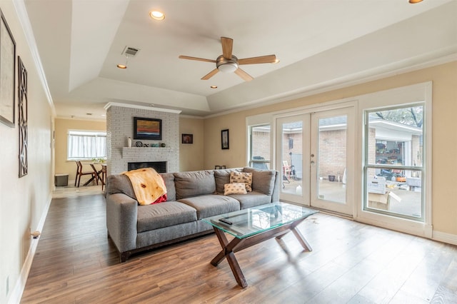 living area featuring a tray ceiling, french doors, visible vents, a brick fireplace, and wood finished floors