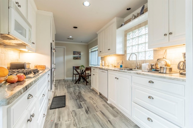 kitchen with light stone counters, white appliances, a sink, white cabinets, and ornamental molding