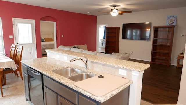 kitchen with dishwasher, light stone counters, open floor plan, a kitchen island with sink, and a sink