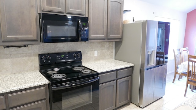 kitchen with black appliances, tasteful backsplash, and light stone counters