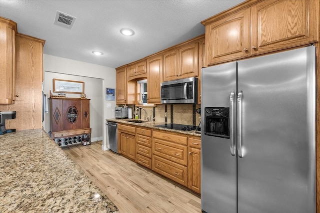 kitchen featuring sink, appliances with stainless steel finishes, light stone countertops, light hardwood / wood-style floors, and decorative backsplash