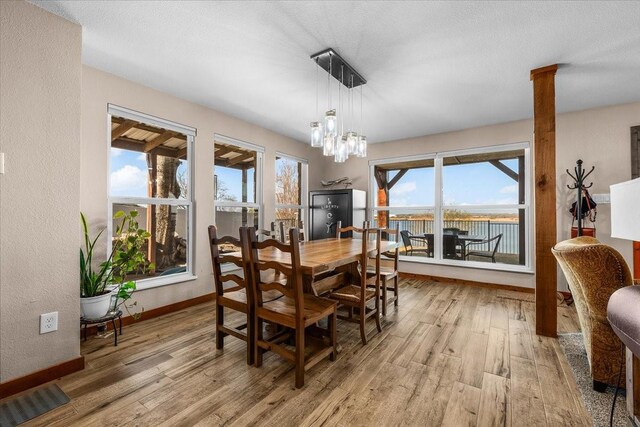 dining space with decorative columns, a water view, a chandelier, and light wood-type flooring