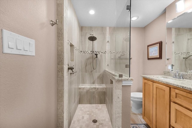 bathroom with tiled shower, vanity, and toilet