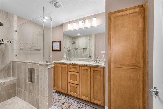 bathroom with double vanity, visible vents, a walk in shower, and a sink