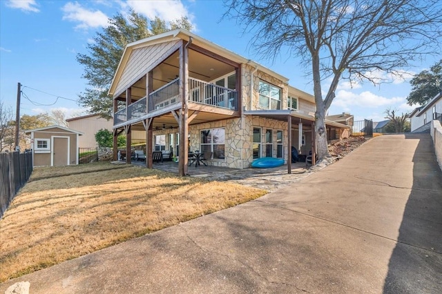 rear view of property featuring a lawn, a storage shed, fence, stone siding, and an outdoor structure