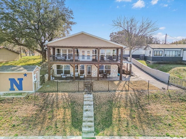 view of front facade with a patio, a fenced front yard, stone siding, and a balcony