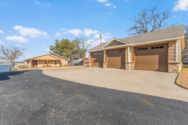 exterior space with a garage, stone siding, an outbuilding, and driveway