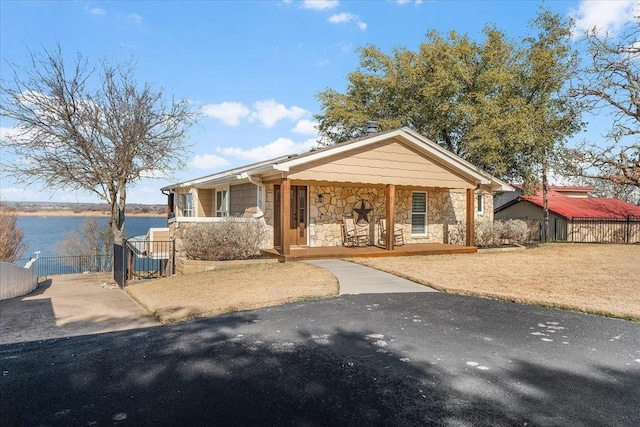 view of front facade with a water view, stone siding, fence, and covered porch