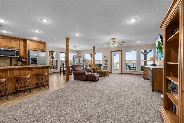 living room featuring ceiling fan, light colored carpet, and ornate columns