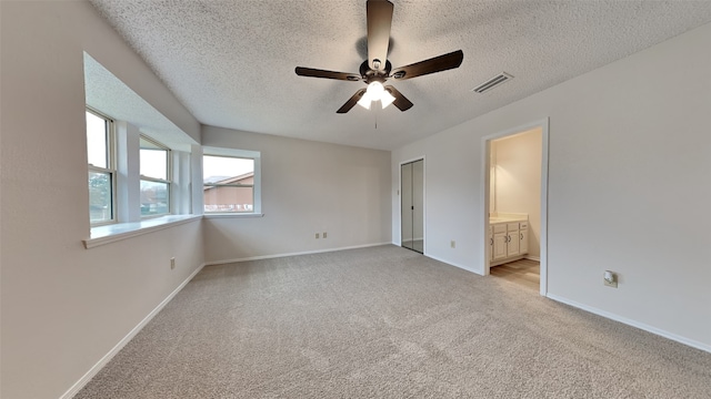 unfurnished bedroom featuring ceiling fan, ensuite bath, light colored carpet, and a textured ceiling