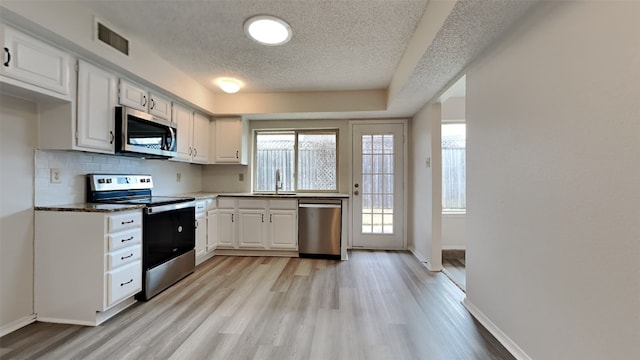 kitchen with stainless steel appliances, white cabinetry, sink, and light hardwood / wood-style flooring