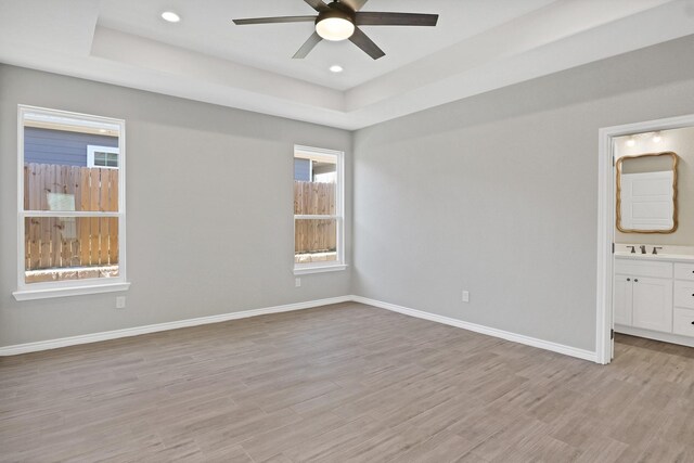 unfurnished bedroom with ceiling fan, a walk in closet, a tray ceiling, and light hardwood / wood-style flooring