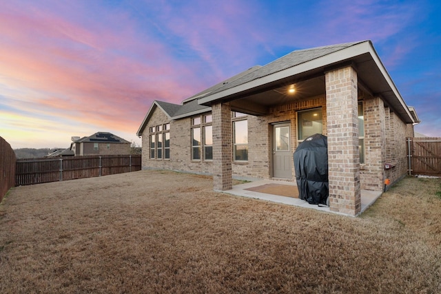 back house at dusk featuring a patio area and a lawn