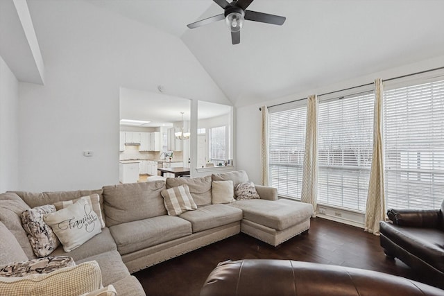 living room with dark wood-type flooring, ceiling fan with notable chandelier, and high vaulted ceiling